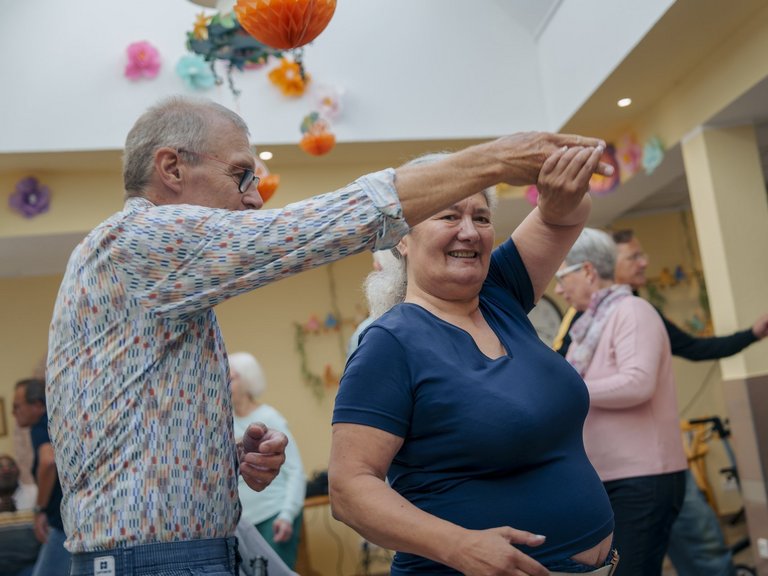 ein Mann mit Brille tanzt mit einer Bewohnerin zusammen und drehen sich