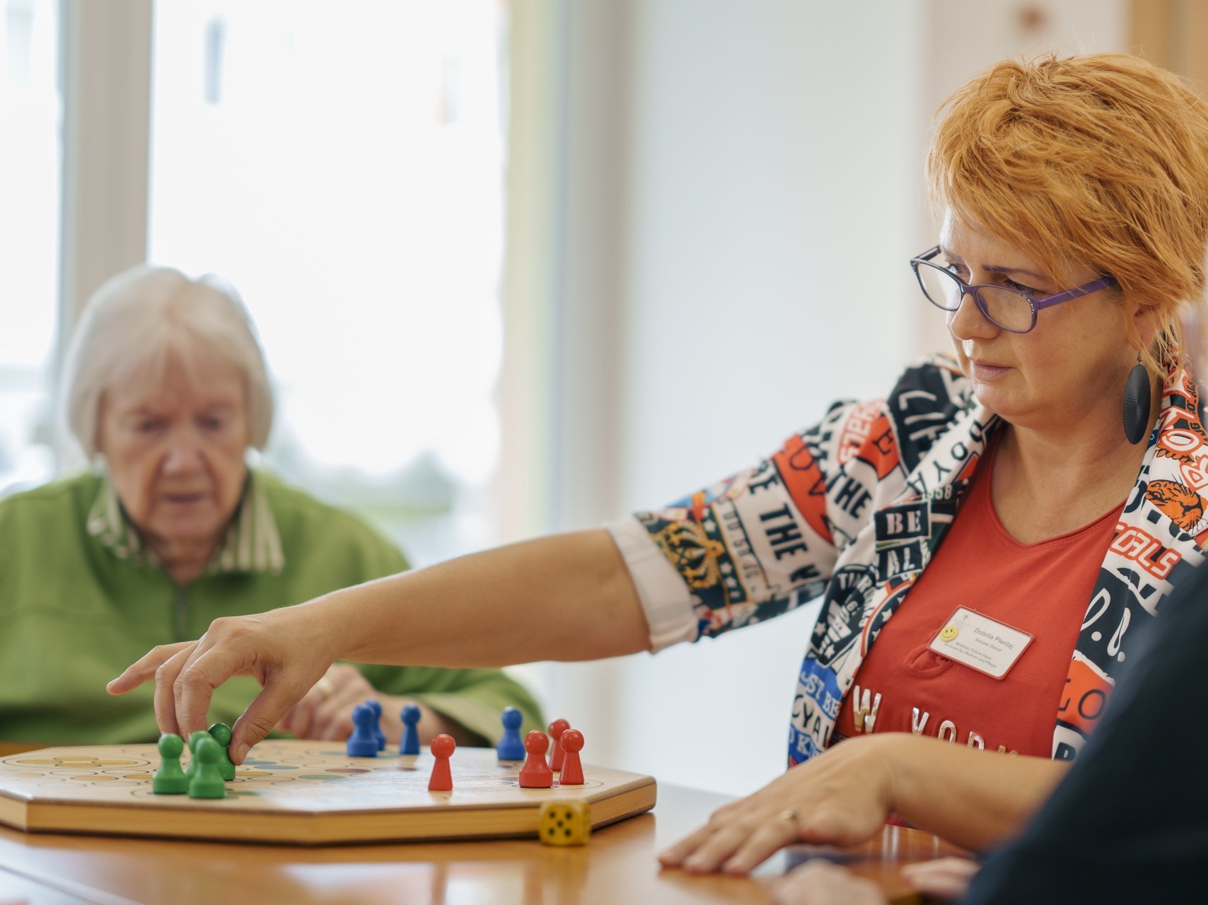 Zwei Bewohnerinnen und eine Pflegekraft spielen zusammen ein Brettspiel  