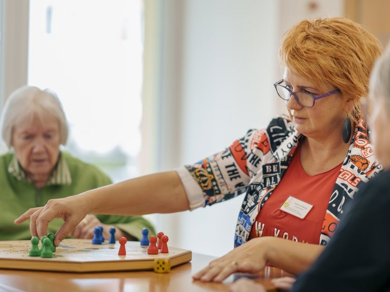 Zwei Bewohnerinnen und eine Pflegekraft spielen zusammen ein Brettspiel  